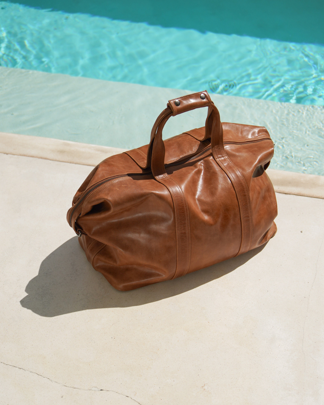 Camel Bare Leather Travel Bag in front of a swimming pool.