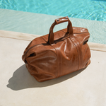 Camel Bare Leather Travel Bag in front of a swimming pool.